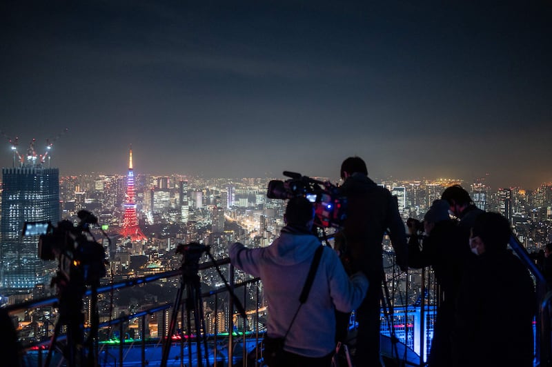 Video journalists document a lunar eclipse from the observation deck on Roppongi Hills, as the Tokyo Tower in the distance is illuminated in honour of Major League Baseball All-Star Japanese player Shohei Ohtani's MVP season, in Tokyo on November 19, 2021.  AFP