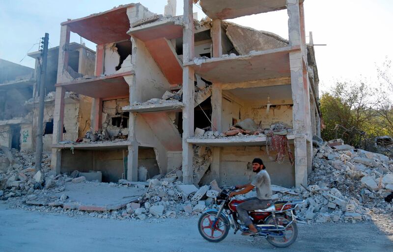 A Syrian man rides a motorcycle past a destroyed building in Jisr Al Shughur in the Idlib province. AFP