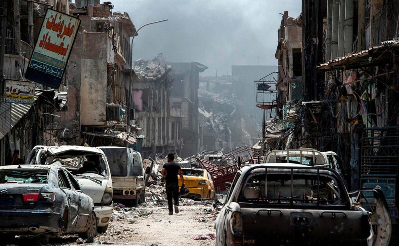 (FILES) In this file photo taken on July 02, 2017 A man walks by destroyed vehicles in a street in the Old City of Mosul on July 2, 2017, during the offensive to retake the city from Islamic State (IS) group fighters. Iraqi forces announced the "liberation" of the country's second city on July 10, 2017, after a bloody nine-month offensive to end the Islamic State (IS) group's three-year rule there. 
Scores of people are still displaced in and around Mosul as the city lies in ruins, one year after it was retaken from IS. 

 / AFP / Fadel SENNA
