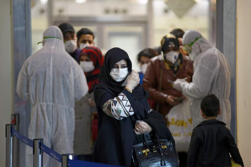 TOPSHOT - Medical staff in protective gears distribute information sheets to Iraqi passengers returning from Iran at Najaf International Airport on March 5, 2020. Iraqi health authorities announced the country's first two deaths from the new coronavirus, one in the capital Baghdad and the other in the autonomous Kurdish region. / AFP / Haidar HAMDANI
