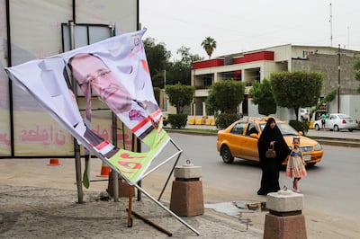 An Iraqi woman and a girl walk past an electoral banner for former Prime Minister Nuri al-Maliki that was damaged by a storm the day before, in the capital Baghdad on April 28, 2018.  / AFP PHOTO / SABAH ARAR