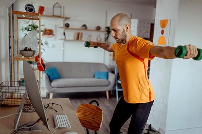 Young man exercising with dumbbells at home, while watching exercise training video online on laptop at home. Getty Images