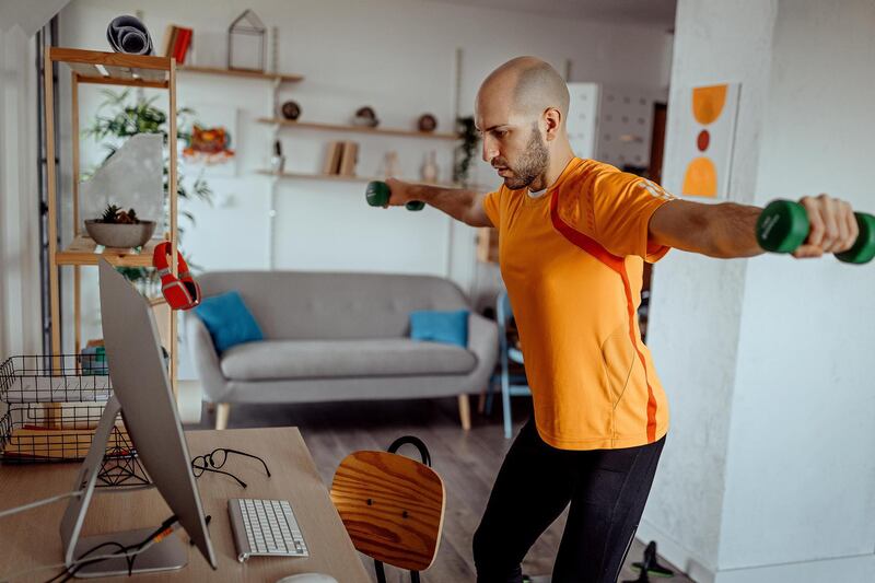 Young man exercising with dumbbells at home, while watching exercise training video online on laptop at home. Getty Images