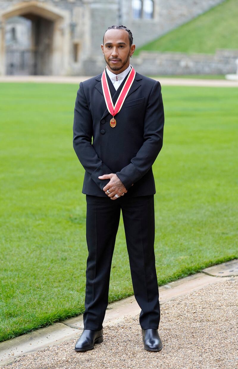 Lewis Hamilton, in a black Wales Bonner suit with a Dior shirt, poses with his medal after being appointed as a knight during a investiture ceremony at Windsor Castle on December 15, 2021.  AFP