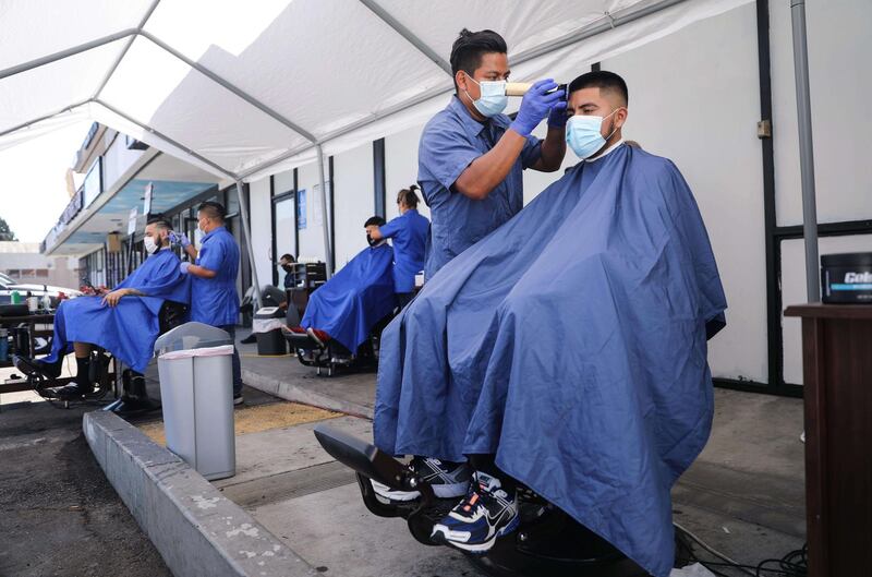 Barbers from King's Cutz give haircuts beneath an awning outside their barbershop while observing safety restrictions in Los Angeles, California.   AFP