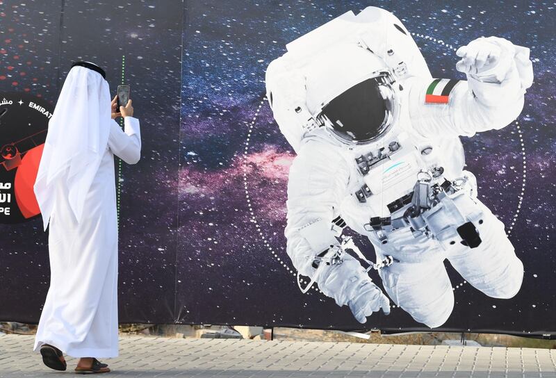 (FILES) In this file photo taken on September 25, 2019 (FILES) In this file photo taken on September 25, 2019 a man takes a picture of an illustration depicting an astronaut with the Emirati national flag outside Mohammed Bin Rashid Space Centre (MBRSC) in Dubai. The first Arab space mission to Mars, set for launch next month to study the Red Planet's atmosphere, is designed to inspire the region's youth and pave the way for scientific breakthroughs, officials said on June 9, 2020.
 / AFP / KARIM  SAHIB
