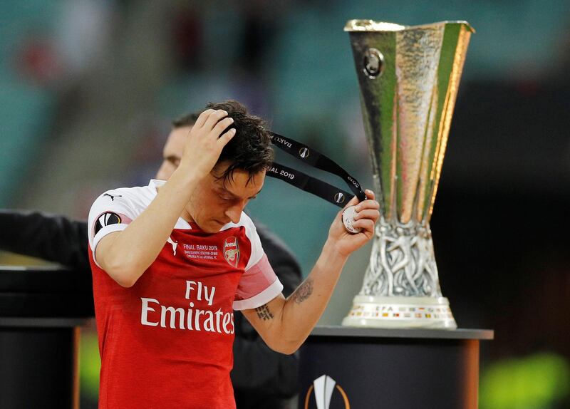 Arsenal's Mesut Ozil looks dejected as he walks past the Europa League trophy after the match. REUTERS