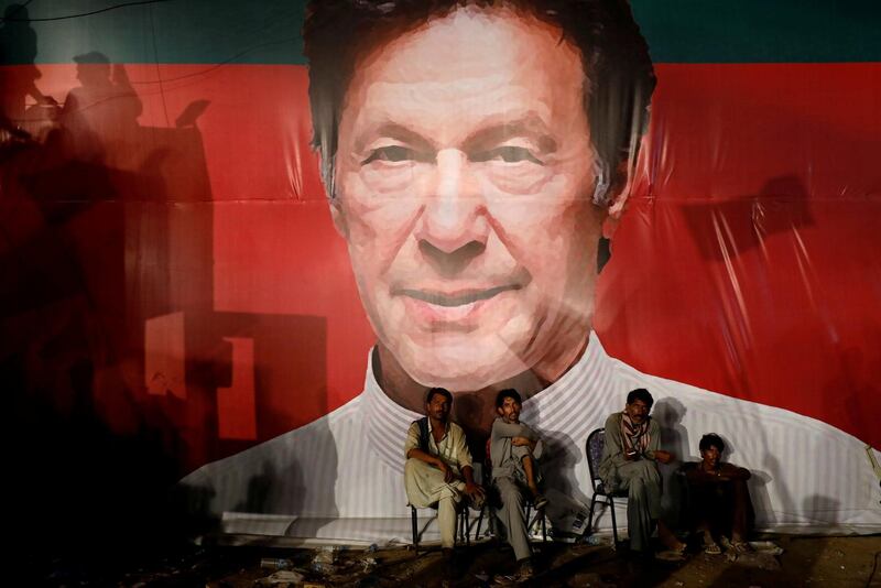 FILE PHOTO: Labourers, who set up the venue, sit under a wall with a billboard displaying a photo of Imran Khan, chairman of the Pakistan Tehreek-e-Insaf (PTI), political party, as they listen to him during a campaign rally ahead of general elections in Karachi, Pakistan July 22, 2018. REUTERS/Akhtar Soomro/File Photo