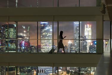 Young woman using smartphone and pulling suitcase, city skyline in view. Getty Images