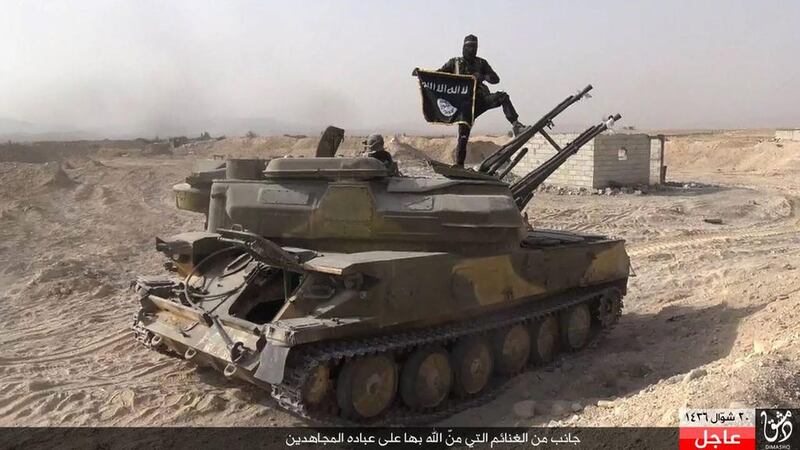 An ISIL militant holds the group's flag as he stands on a tank captured from Syrian government forces, in the town of Qaryatain southwest of Palmyra. Rased News Network via AP Photo