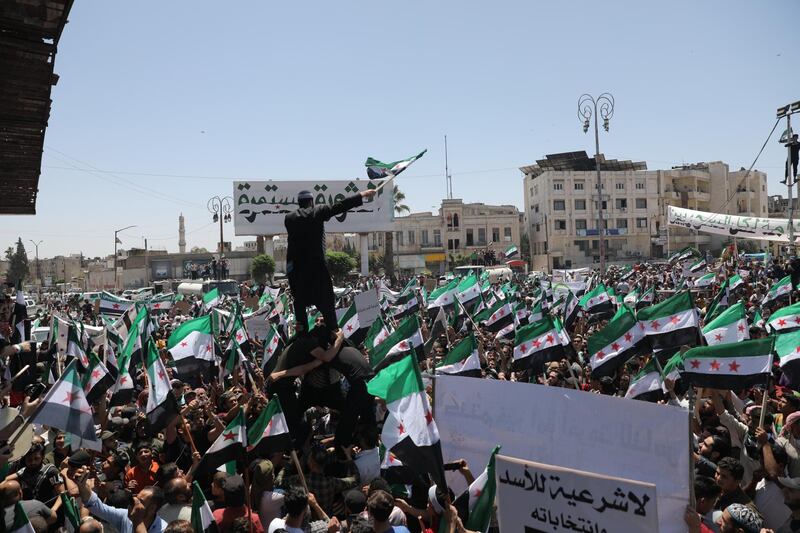 Syrian people hold placards and the Syrian opposition factions' flags as they gather under a banner reading in Arabic 'revolution continues' during a protest against the presidential elections, in Idlib, Syria. EPA