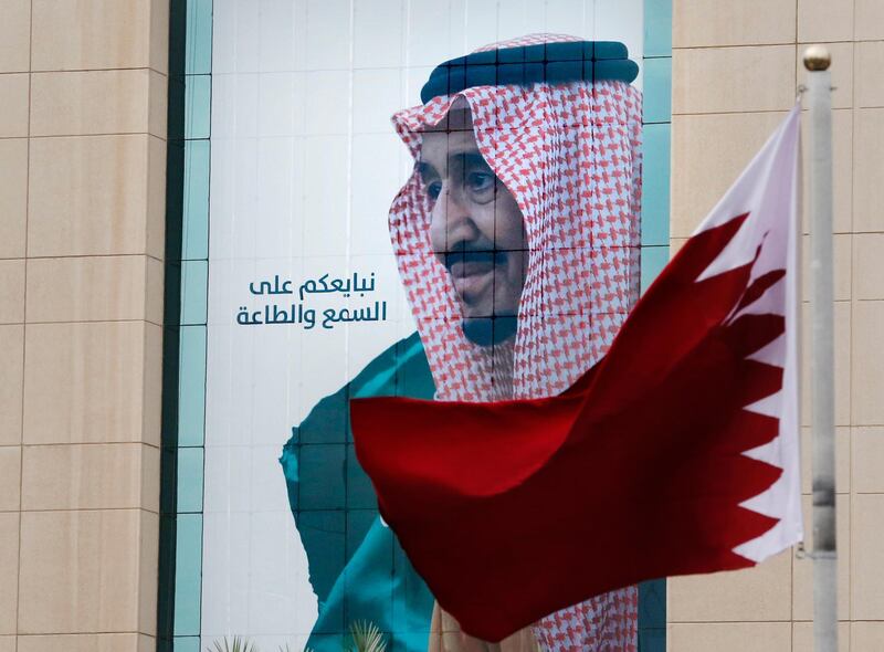 A Qatari flag flies in front of a banner showing Saudi King Salman with Arabic reads, "We pledge you to listen and obey" at a trade center in Riyadh, Saudi Arabia, Monday, Dec. 9, 2019 ahead of the Gulf Cooperation Council "GCC", 40th summit. (AP Photo/Amr Nabil)