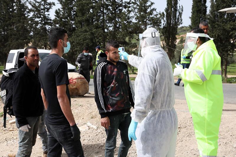 Palestinian health ministry workers check the temperatures of men crossing the Tarqumiya checkpoint, near Hebron, West Bank, on March 27, 2020. EPA