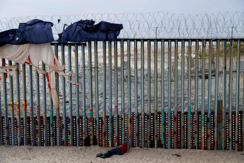 A man sleeps next to the US border wall topped with razor wire in Tijuana, Mexico. AP Photo