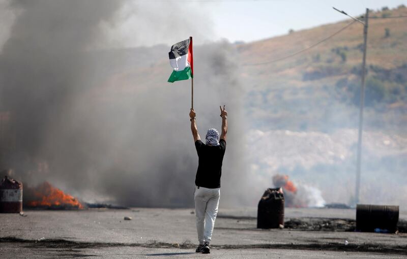 A demonstrator holding a Palestinian flag gestures during a protest over tension in Jerusalem and Israel-Gaza escalation, near Hawara checkpoint near Nablus in the Israeli-occupied West Bank, May 14, 2021. REUTERS/Raneen Sawafta