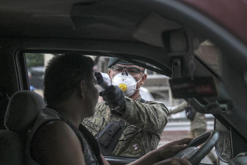 A member of the Philippine Army wearing a protective mask takes the temperature of the driver of a vehicle, traveling into Metro Manila, at a check point on Mindanao Avenue. Bloomberg