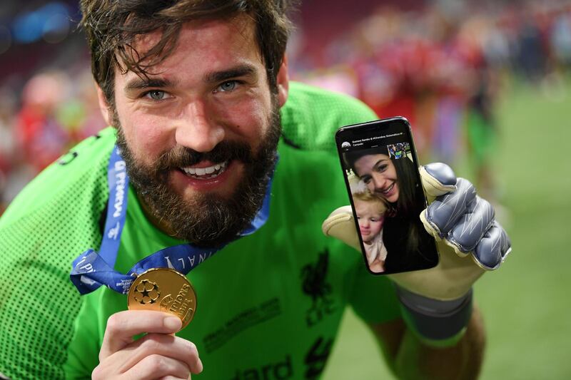 Alisson of Liverpool celebrates with his phone on the pitch after helping his side become winners. Getty
