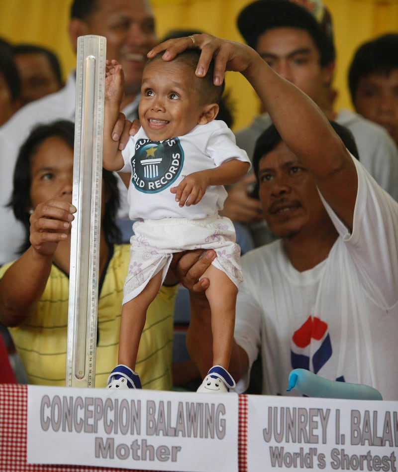 Junrey Balawing, 18, smiles as he stands next to a ruler being held by his mother Concepcion prior to the last of a series of measurements conducted by Guinness World Records at Sindangan Municipal Hall in Sindangan township, Zamboanga Del Norte province in Southern Philippines, Sunday June 12, 2011. Balawing was officially declared 'the world's shortest living man' with a measurement of 59.93 Centimeters (23.5 inches) dislodging Nepal's Khagendra Thapa Magar with a measurement of 26.4 inches. At right is Junrey's father Reynaldo. (AP Photo/Bullit Marquez) *** Local Caption ***  XBM108_APTOPIX_Philippines_Shortest_Man.jpg