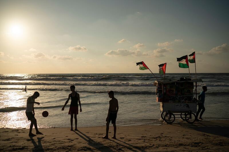 A vendor pulls his snack cart decorated with Palestinian flags as boys play soccer on the beach before sunset in Gaza City. AP