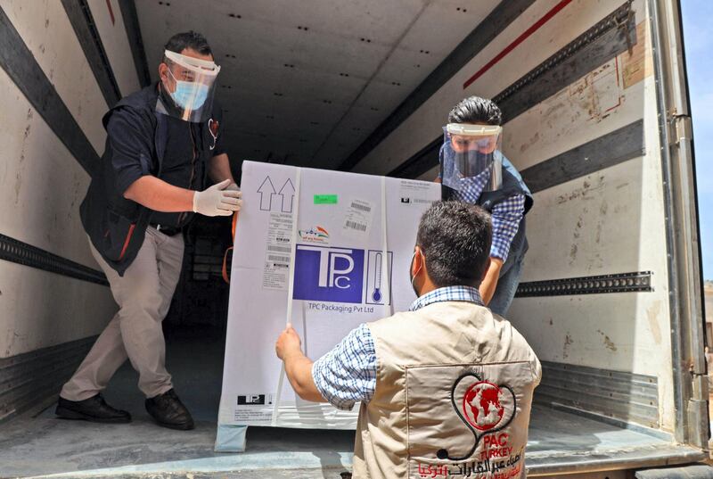 Staff of the Physicians Across Continents group unload the first batch of AstraZeneca COVID-19 vaccines at Bab al-Hawa border crossing between Syria and Turkey in Syria's rebel-held northwestern Idlib on April 21, 2021. The 53,800 AstraZeneca doses were dispatched to the rebel-dominated region as part of the Covax programme, which aims to ensure equitable access to Covid vaccinations. / AFP / Mohammed AL-RIFAI

