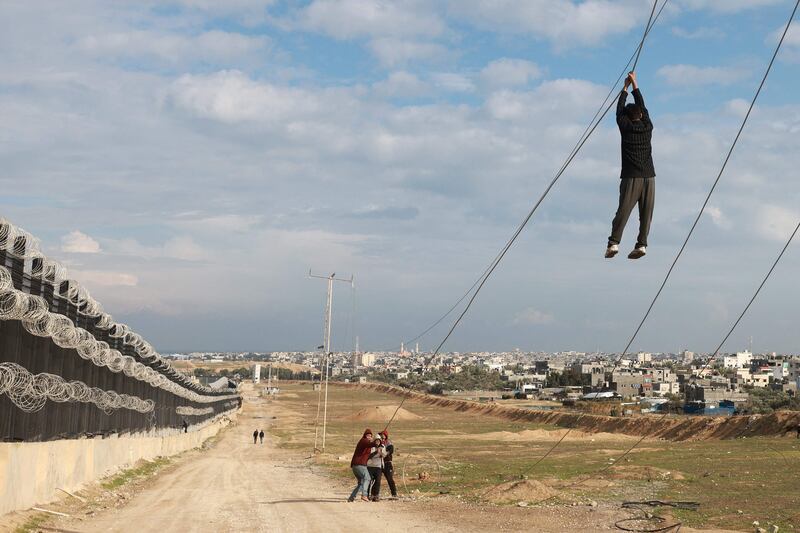 Displaced Palestinian children play with a non functioning electricity cable near the border fence between Gaza and Egypt, on February 16, 2024 in Rafah, in the southern Gaza Strip, amid the ongoing conflict between Israel and the Palestinian Hamas militant group.  Nearly 1. 5 million displaced Palestinians are trapped in Rafah -- more than half of Gaza's populations -- seeking shelter in a sprawling makeshift encampment near the Egyptian border.  (Photo by MOHAMMED ABED  /  AFP)