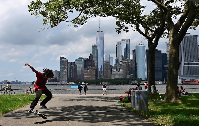 A man skateboards with the Manhattan skyline visible in the distance as people visit Governors Island on July 15, 2020 in New York City. - The 172-acre island located in New York Harbor reopened to visitors with limited capacity due to continued concerns over the coronavirus pandemic. (Photo by Angela Weiss / AFP)