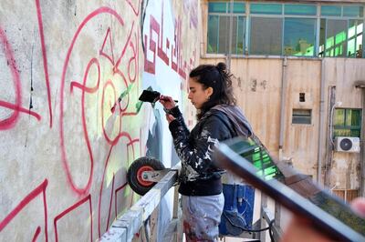 Artist Miramar Al Nayyar uses the red markers on the wall and the image on her phone to paint the final design on to the eight-storey building. Muhammad Emad