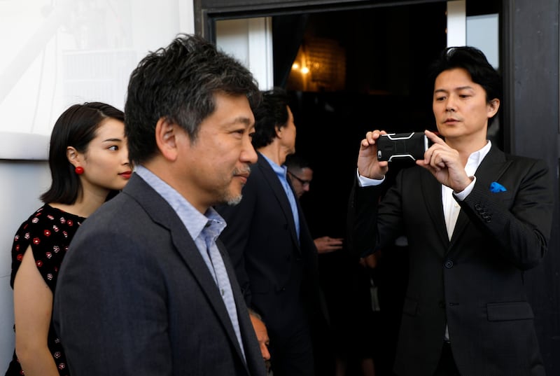 Actor Fukuyama Masaharu, right, films with his phone as director Kore-eda Hirokazu walks in front of him as he arrives for the photo call of the film Sandome No Satsujin (The Third Murder) AP Photo / Domenico Stinellis