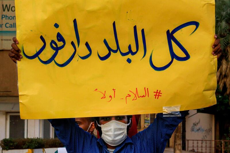(FILES) In this file photo taken on July 4, 2020, A mask-clad demonstrator (due to the COVID-19 coronavirus pandemic) stands with a sign reading in Arabic "all of the country is Darfur, #PeaceFirst", during a protest outside the Sudanese Professionals Association in the Garden City district of Sudan's capital Khartoum, in solidarity with the people of the Nertiti region of Central Darfur province in the country's southwest. Ongoing clashes in Sudan's restive Darfur have killed at least 48 people in two days, state media said, just over two weeks after a long-running peacekeeping mission ended operations. The violence has pitted the Massalit tribe against Arab nomads in El Geneina, the capital of West Darfur state, but later morphed into broader fighting involving armed militias in the area. / AFP / ASHRAF SHAZLY

