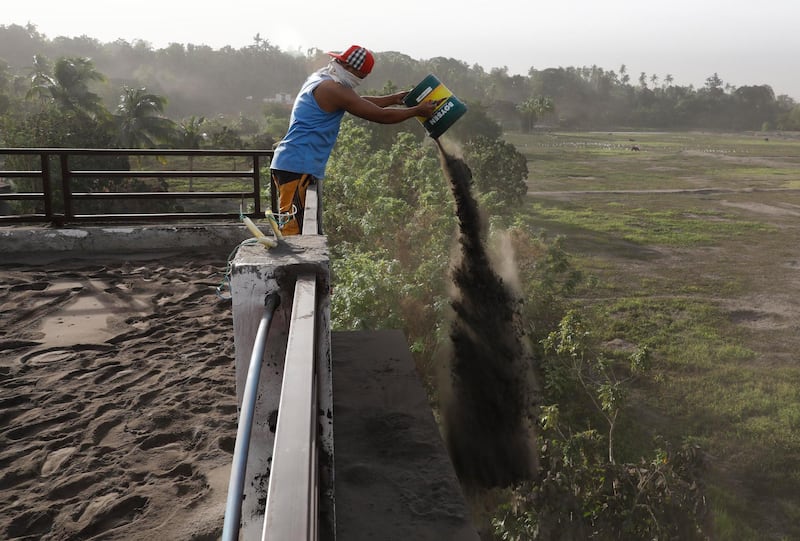 A man throws out ash deposits that accumulated on the roof of his home, a day after the eruption of Taal Volcano, in Agoncillo town in Batangas. EPA