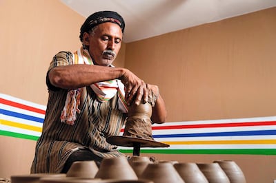 A potter works at his craft. In the background, you can see the colours that houses are traditionally painted in the region. Courtesy of Saudi MOC