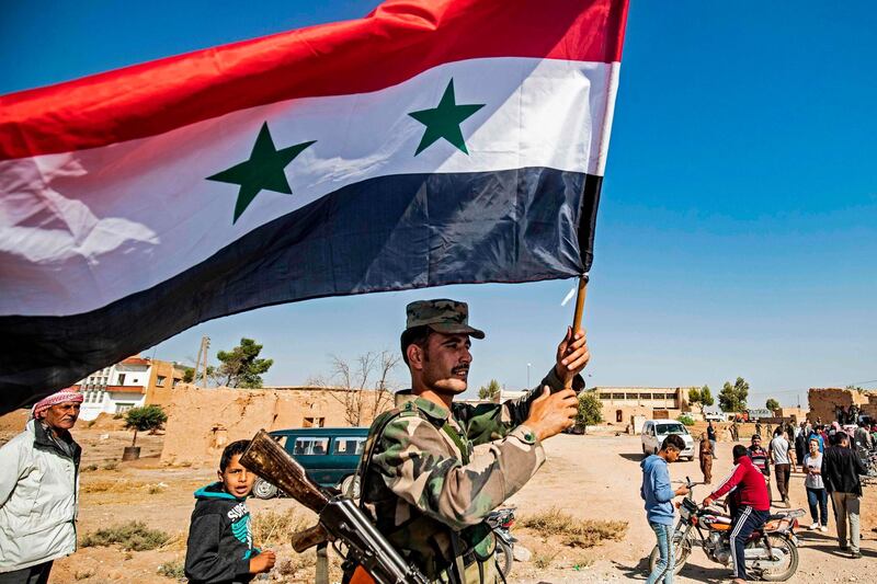 TOPSHOT - A Syrian regime soldier waves the national flag a street on the western entrance of the town of Tal Tamr in the countryside of Syria's northeastern Hasakeh province on October 14, 2019. Syrian regime forces moved towards the Turkish border Monday after Damascus reached a deal with beleaguered Kurdish forces following a US withdrawal announcement, AFP correspondents reported. Soldiers waving Syrian flags deployed west of Tall Tamr, not far from the flashpoint border town of Ras al-Ain, which has been a key target of Turkish forces and their proxies since they launched their onslaught six days ago. / AFP / Delil SOULEIMAN
