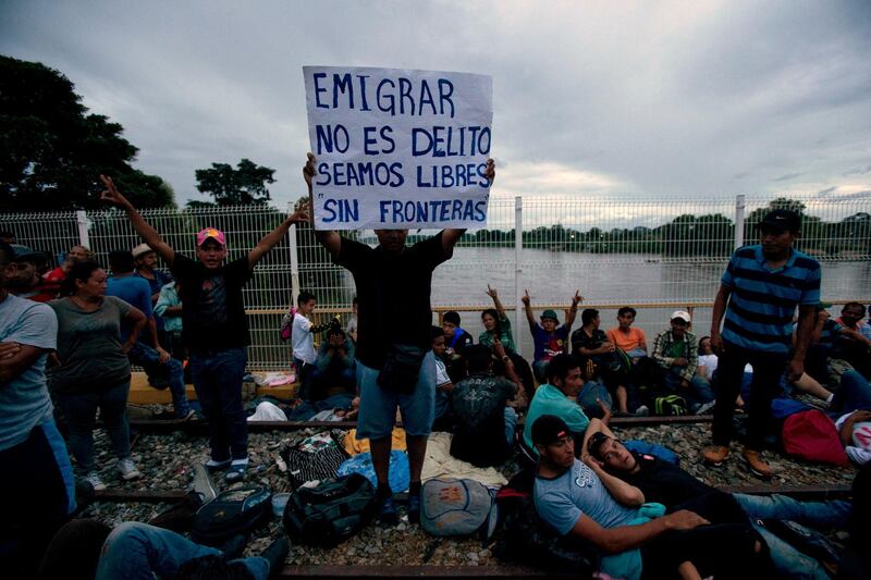 A migrant bound for the U.S.-Mexico border holds up a sign with a message that reads in Spanish: "To emigrate is not a crime, let's be free, without borders," on a bridge that stretches over the Suchiate River, connecting Guatemala and Mexico, in Tecun Uman, Guatemala, Friday, Oct. 19, 2018. The entry into Mexico via the bridge has been closed. The U.S. president has made it clear to Mexico that he is monitoring its response. On Thursday he threatened to close the U.S. border if Mexico didn't stop the caravan. (AP Photo/Moises Castillo)