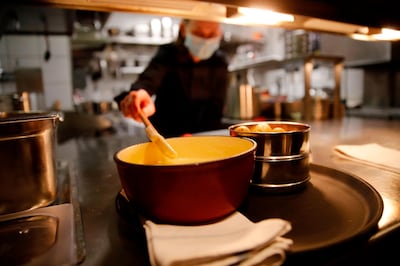 A cooker wearing a protective face mask prepare a fondue, the beloved Swiss national dish of cheese melted down with white wine in a "caquelon" pot heated by an open flame at Restaurant Marzilibruecke in Bern, on November 16, 2020.

 As Switzerland contends with one of the worst coronavirus surges in Europe, the Swiss are gripped by one melting hot question: is it still safe to share a fondue? - TO GO WITH AFP STORY BY AGNES PEDRERO AND VIDEO BY ELOI ROUYER
 / AFP / STEFAN WERMUTH / TO GO WITH AFP STORY BY AGNES PEDRERO AND VIDEO BY ELOI ROUYER
