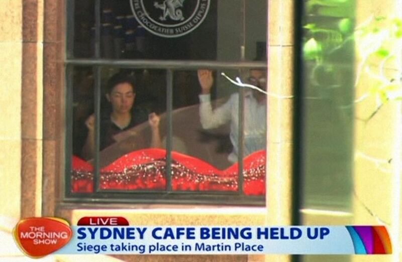 This image taken from video shows people holding up their hands inside the cafe in Sydney, Australia on Monday. A gunman took an unknown number of people hostage inside the downtown Sydney chocolate shop and cafe at the height of Monday morning rush hour, with two people inside the cafe seen holding up a flag believed to contain an Islamic declaration of faith. AP Photo / Channel 7 via AP Video
