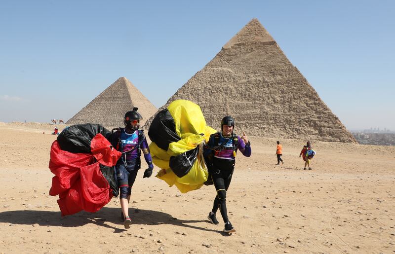 Skydivers carry their parachutes in front of the pyramids.