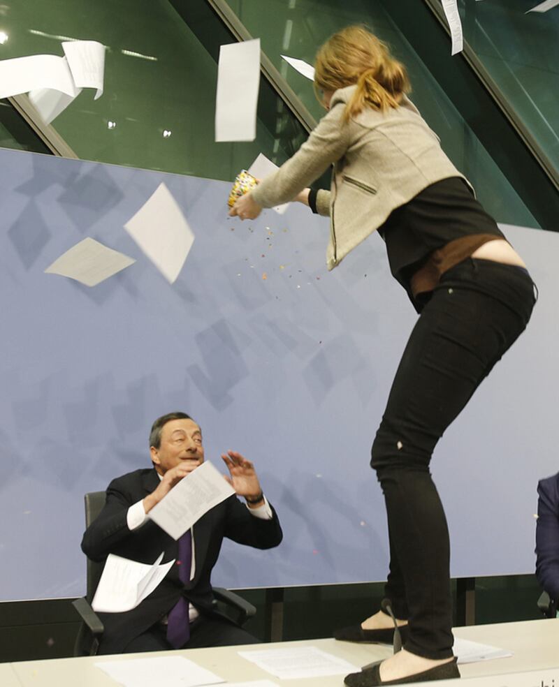 The Femen activist stands on the table of the podium and throws paper at ECB president Mario Draghi. Michael Probst / AP Photo