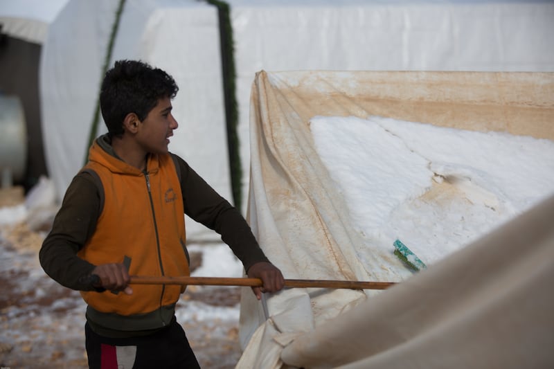 Faisal, 13, scrapes snow off his tent. He says he loves snow and playing in it with his friends, but the winter has become a tragedy for his family as their tent was destroyed in the storm. In his home village, he used to have fun when it snowed, but now he is sad.