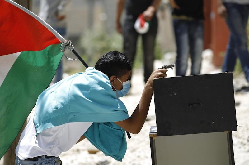 A Palestinian protester, holding the Palestinian flag, uses a toy gun during clashes with Israeli troops over the controversial Israeli barrier in Kfar Aqab near the West Bank city of Ramallah. Mohamad Torokman / Reuters