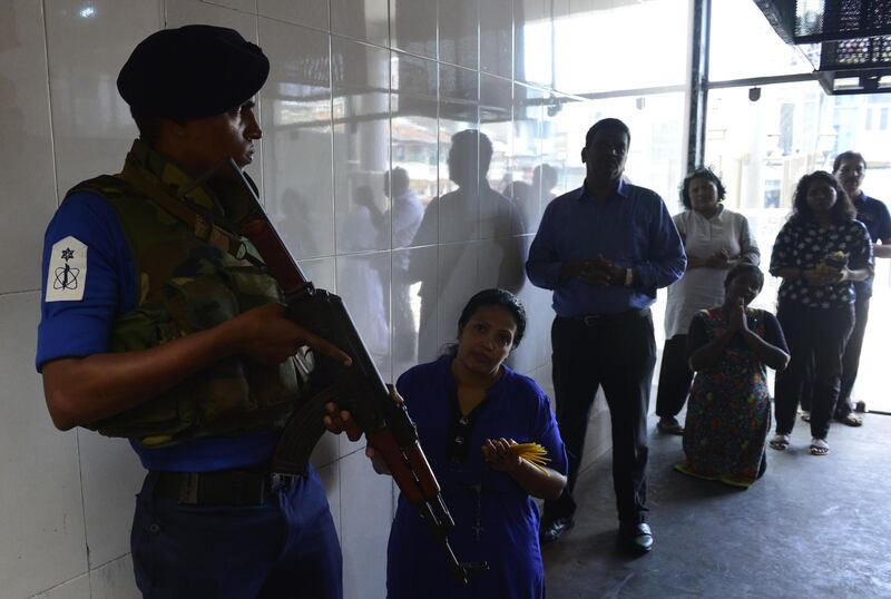 A Sri Lankan Navy personnel stands guard as Catholic devotees pray at St. Anthony's church after it was partially opened for the first time since the Easter Sunday attacks in Colombo on May 7, 2019. Sri Lanka's iconic St. Anthony's church partially opened for worship May 7 even as security forces were rebuilding a shine inside following the Easter suicide bombing. / AFP / LAKRUWAN WANNIARACHCHI

