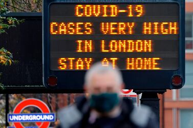 Pedestrians walk past a sign alerting people that "COVID-19 cases are very high in London - Stay at Home". AFP
