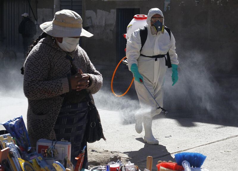 A municipal worker sprays disinfectant past a street vendor at a market in Puno, Peru. AFP