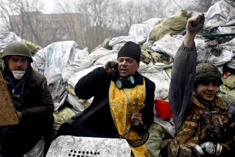 An Orthodox priest talks on the phone as anti-government protesters pause on a barricade. Fierce clashes between police and protesters, some including gunfire, shattered a brief truce, killing numerous people. Marko Drobnjakovic / AP photo