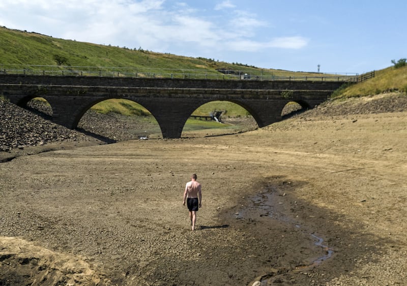 A man walks along a dry bank of a tributary to the Dowry Reservoir close to Oldham. PA