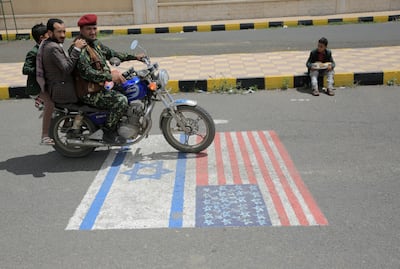 Houthi supporters ride a motorcycle over US and Israeli flags during a protest in Sanaa. EPA