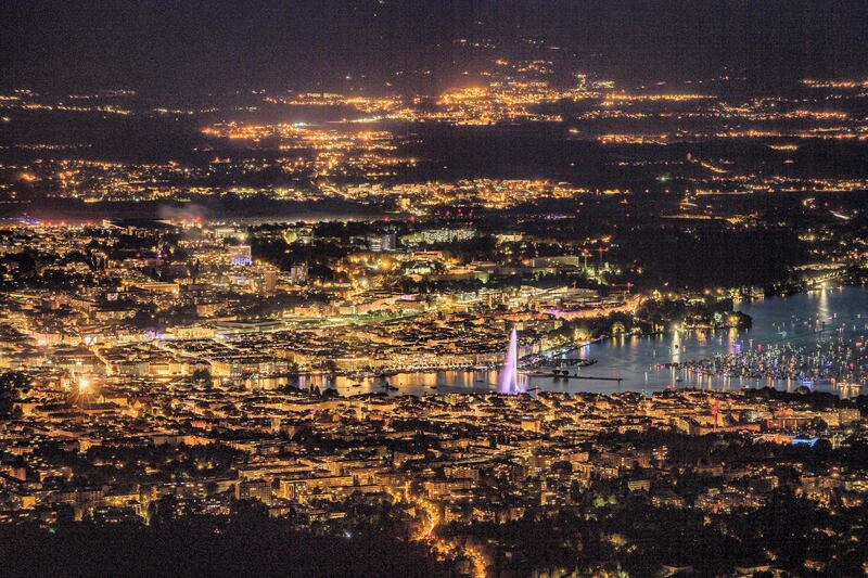 This photograph taken late August 11, 2018, from the French mountain of Saleve shows a nightime view of the city of Geneva at the end of Lake Geneva with its landmark Fountain which is known as "Jet d'Eau". (Photo by Fabrice COFFRINI / AFP)