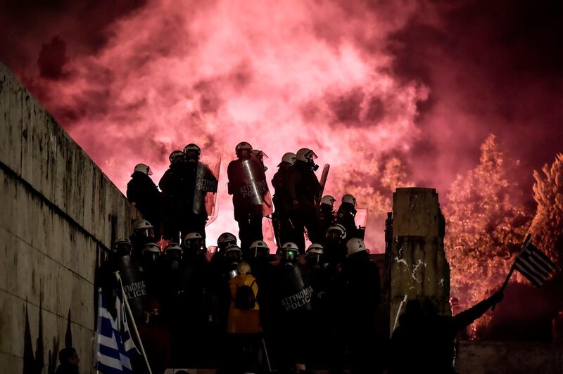 Riot police stand guard outside the Greek parliament in Athens as protesters throw flares during a demonstration against an agreement to rename Greece's neighbour Macedonia as the Republic of North Macedonia. AFP