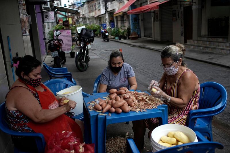 Women peel potatoes outside a snack bar amid the new coronavirus pandemic in Rio de Janeiro, Brazil, October 9, 2020. Silvia Izquierdo / AP