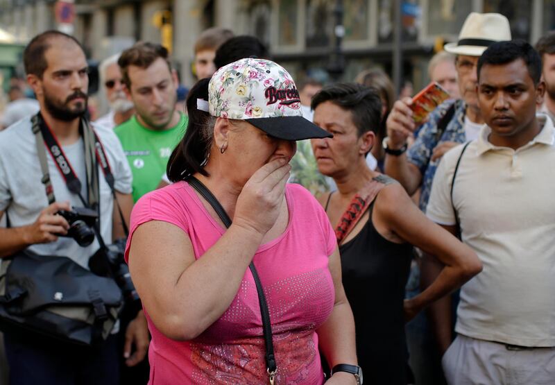 A woman covers her mouth as people gather in Las Ramblas, Barcelona, Spain, Friday, Aug. 18, 2017. Spanish police on Friday shot and killed five people carrying bomb belts who were connected to the Barcelona van attack that killed at least 13, as the manhunt intensified for the perpetrators of Europe's latest rampage claimed by the Islamic State group.(AP Photo/Manu Fernandez)