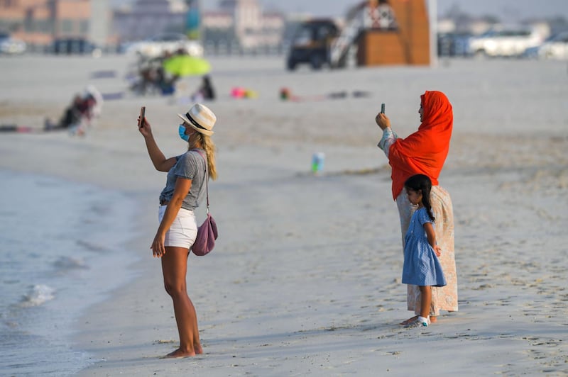 An Emirati woman and a foreign resident, clad in mask due to the COVID-19 coronavirus pandemic, use their phones to take a picture as they stand along a beach in the Gulf Emirate of Dubai on June 25, 2020.  / AFP / KARIM SAHIB
